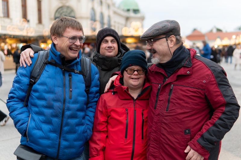 Vier Freunde stehen lachend Arm in Arm auf einem Adventmarkt.