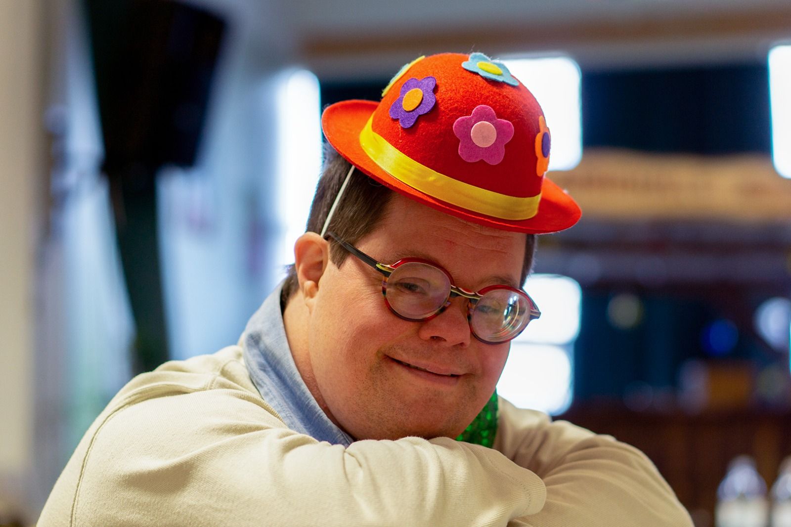 Ein junger Mann mit Brille und buntem Blumenhut lächelt in die Kamera.